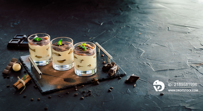 Three portions of sweet tiramisu in glass on dark background. Space for text