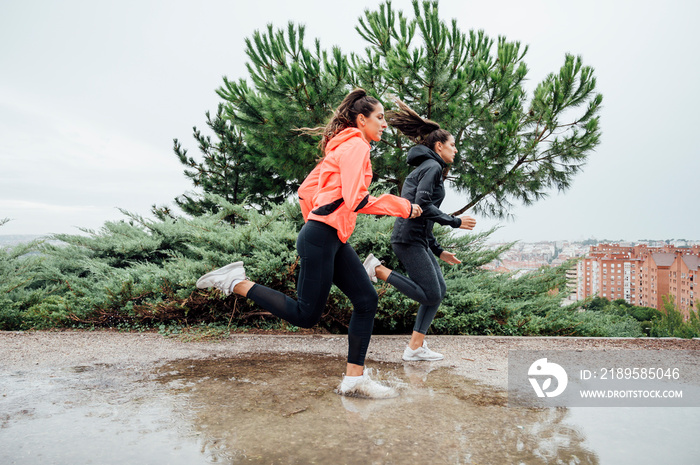 两个美丽的女人在雨水和水坑的公园里奔跑。