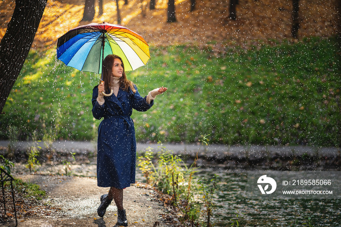 年轻美丽、快乐微笑的女孩撑着伞在雨中摆姿势的户外肖像