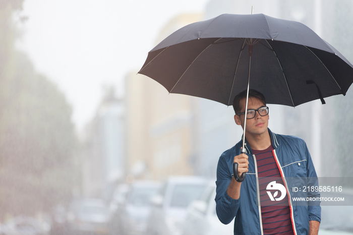 Young man with umbrella on rainy city street