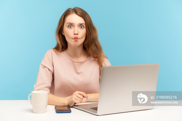 Funny comical woman employee sitting at workplace with laptop and making humorous fish face grimace 