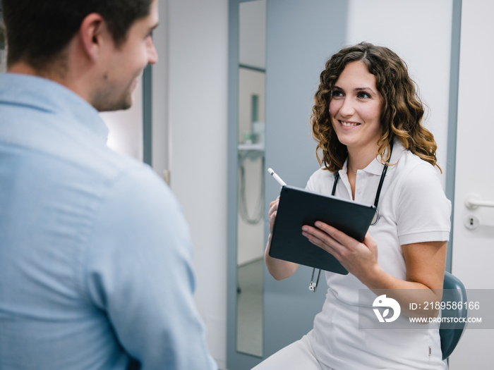 Junge Ärztin geht den Anamnesebogen mit einem neuen Patienten durch