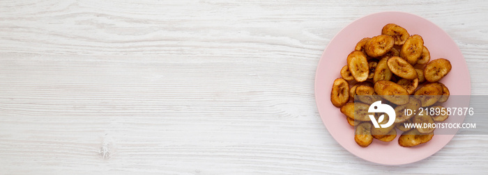 Homemade fried plantains on a pink plate over white wooden background, view from above. Flat lay, to