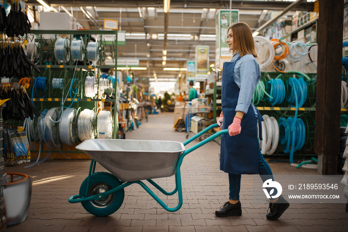 Female seller in apron holds garden cart in shop