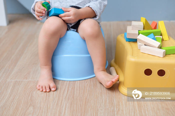 Closeup of legs of cute little Asian 18 months old toddler baby boy child sitting on potty playing w