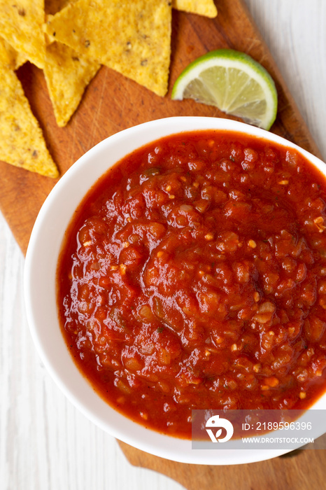 Homemade Tomato Salsa and Nachos on a rustic wooden board on a white wooden background, top view. Fl