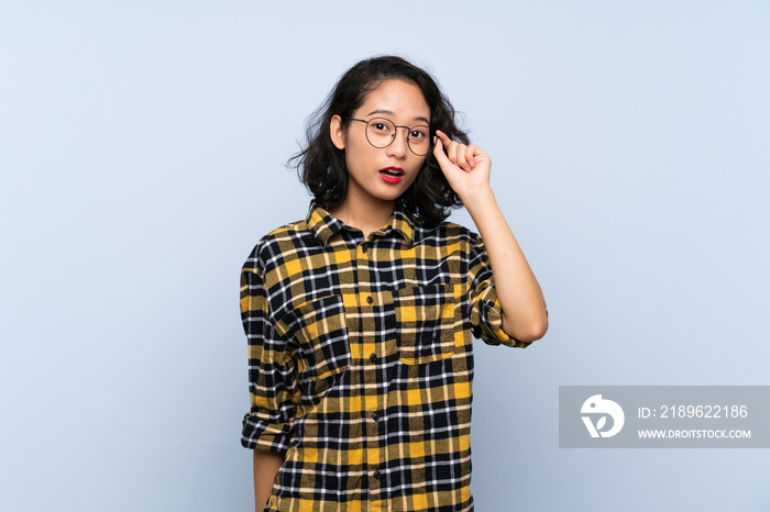 Asian young woman over isolated blue background with glasses and surprised