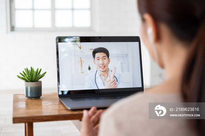 亚洲女性通过电脑笔记本电脑虚拟视频通话或视频会议与医生交谈，远程治疗