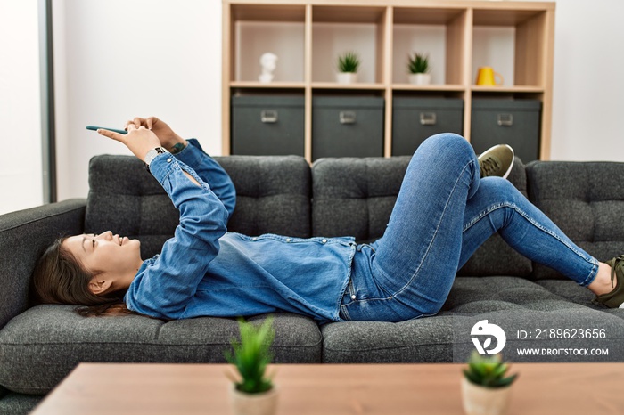 Young chinese girl using smartphone lying on the sofa at home.