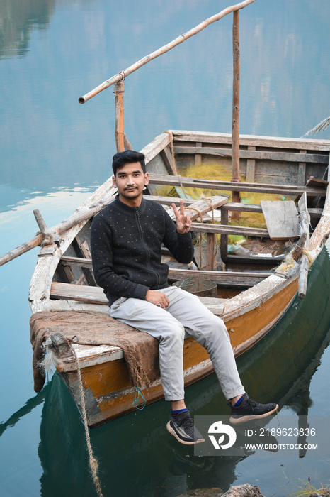 Guy sitting on fishing boat legs hanging and posing  v  gesture