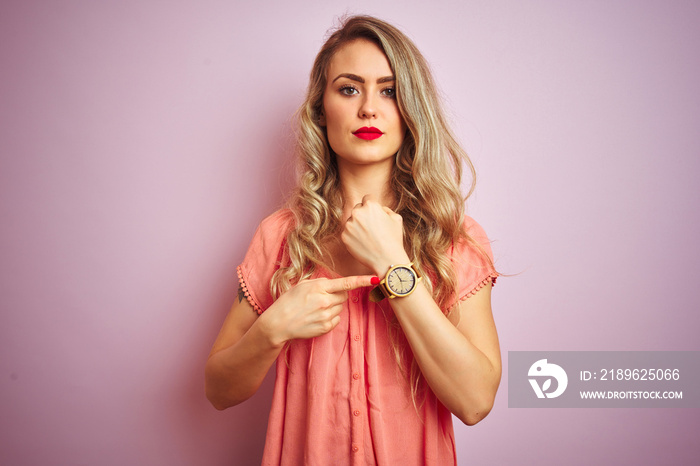 Young beautiful woman wearing t-shirt standing over pink isolated background In hurry pointing to wa