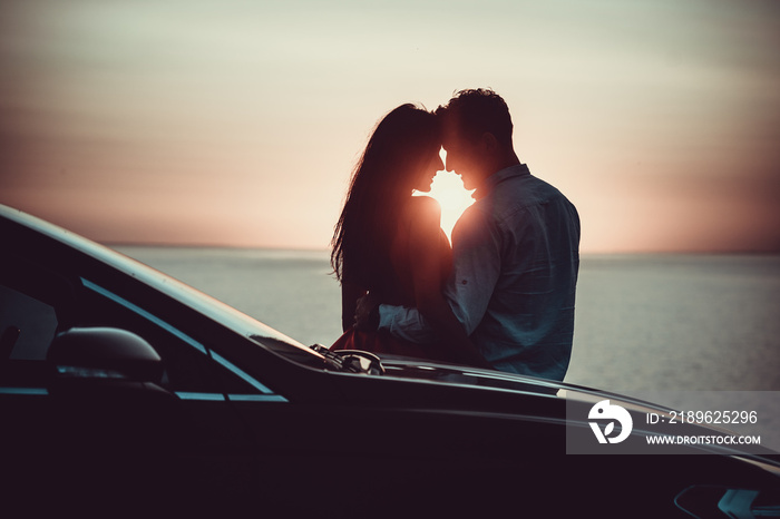 The romantic couple standing near the car on the beautiful sunset background