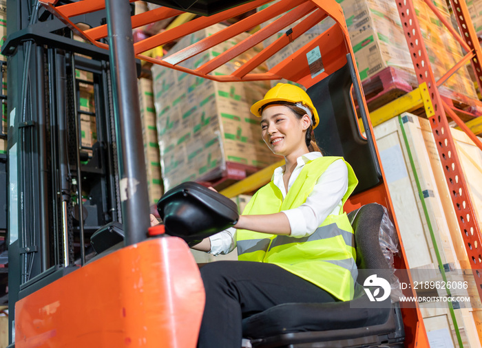 Forklift driver asian young woman in safety jumpsuit uniform with yellow hardhat at warehouse. Worke