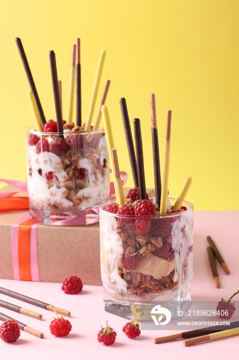 Two glasses with chocolate granola, banana and raspberry, decorated with sticks Pocky on yellow and 