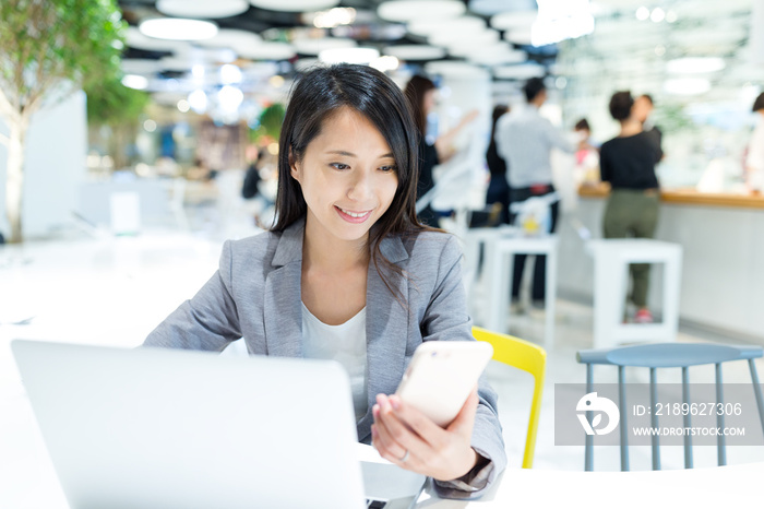 Businesswoman looking at the cellphone with her laptop computer