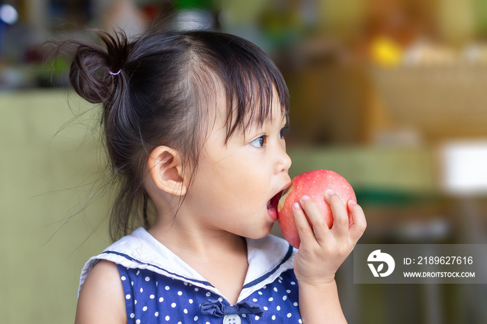 Portrait​ image​ of​ 1-2​ yeas​ old​ of​ baby.​ Happy​ Asian child girl eating and biting a​ red app