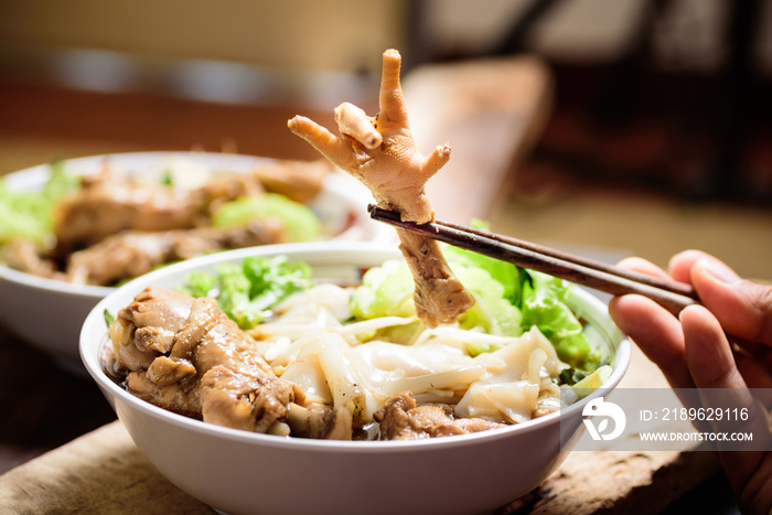 Hand holding chopsticks for eating stewed chicken feet in rice noodles soup