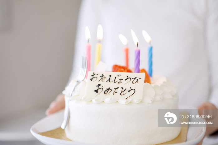 日本語で誕生日おめでとうと書かれているケーキを運ぶアジア人のお母さん