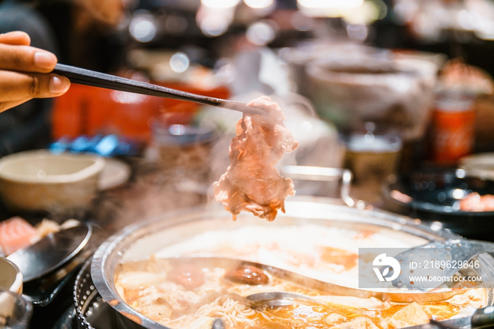 用筷子从火锅麻辣汤底中捏出煮好的中熟和牛A5牛肉片。