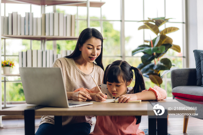 母亲和亚洲孩子小女孩学习和看着笔记本电脑做家庭作业学习kn