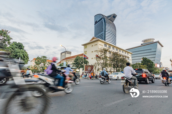 People driving motorbikes on the street in Phnom Penh, Cambodia. Modern skyscrapers on the backgroun