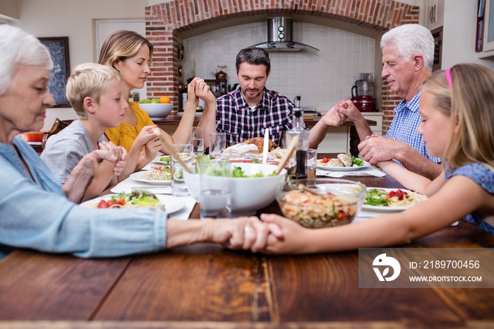 Multi-generation family praying before having meal