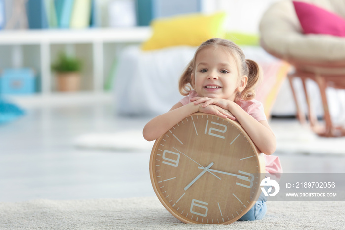 Cute little girl with big clock sitting on floor at home