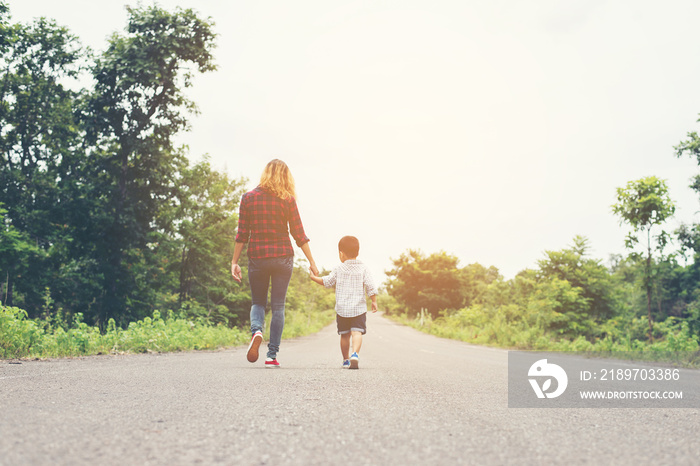 Mother holding a hand of his son in summer day walking on the st