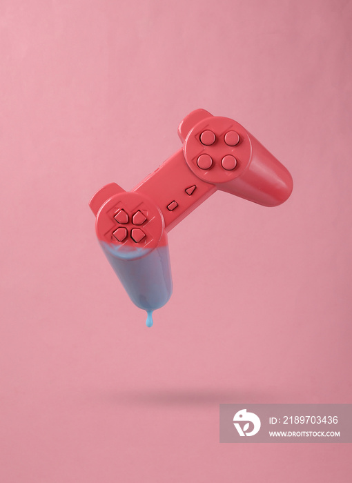 Levitating gamepad with dripping turquoise paint on a pink background. Minimal creative layout. Conc