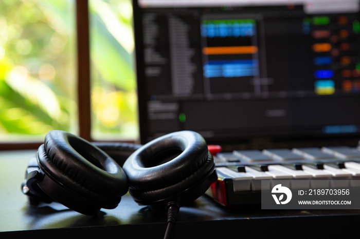 Close up of professional headphones and a Midi keyboard in a music producer home studio. Laptop and 