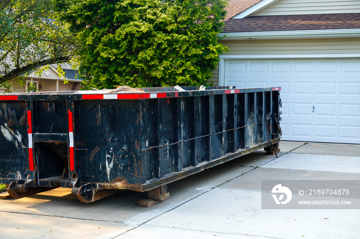 Long blue dumpster full of wood and other debris in the driveway in front of a house in the suburbs 