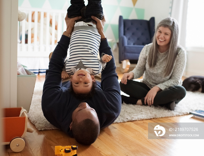 Happy mother looking at playful father picking up son upside down while sitting in room