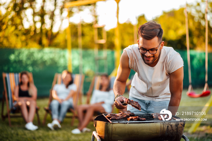 Young positive man grilling meat on a barbecue outdoors, for friends.