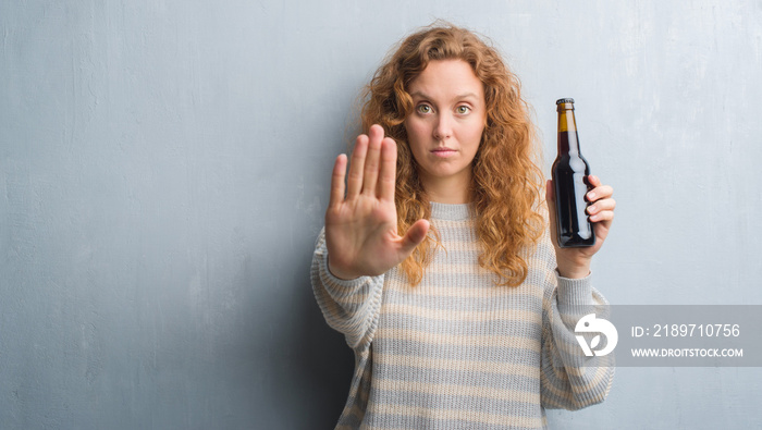 年轻的红发女人在灰色垃圾墙上张开手拿着啤酒瓶，用se做停车标志
