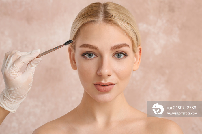 Young woman undergoing eyebrow correction procedure on color background