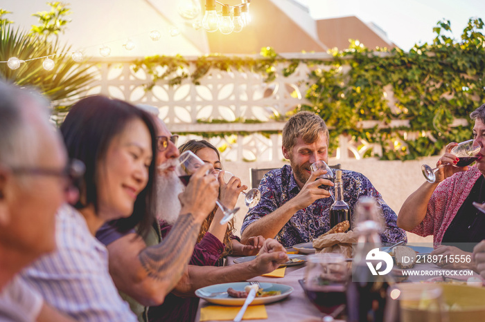 Happy family eating and drinking wine at barbecue dinner on patio outdoor - Mature and young people 