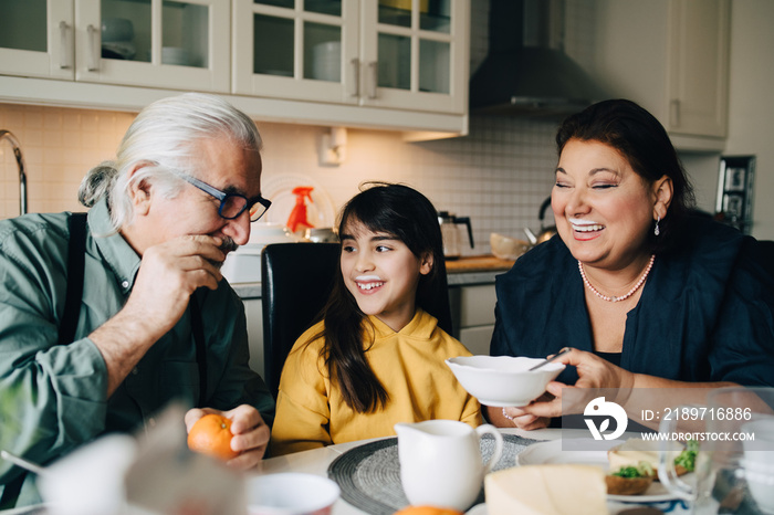 Senior man talking to woman and grandchild with milk mustache during breakfast at kitchen