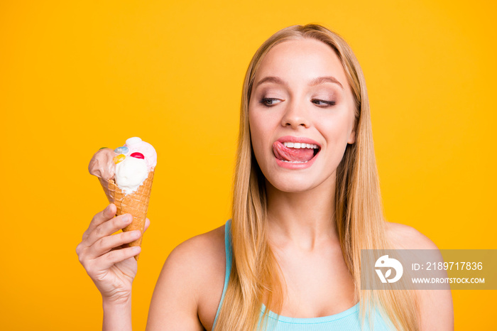 Close up of beautiful blond girl looks at the ice cream cone in her hand and pops out a tongue to ta