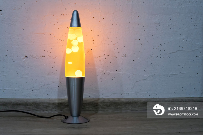 Orange lava lamp stands near a white wall