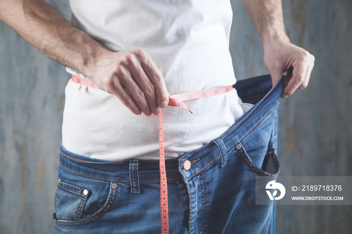 Man measure his belly and showing big jeans. Losing weight