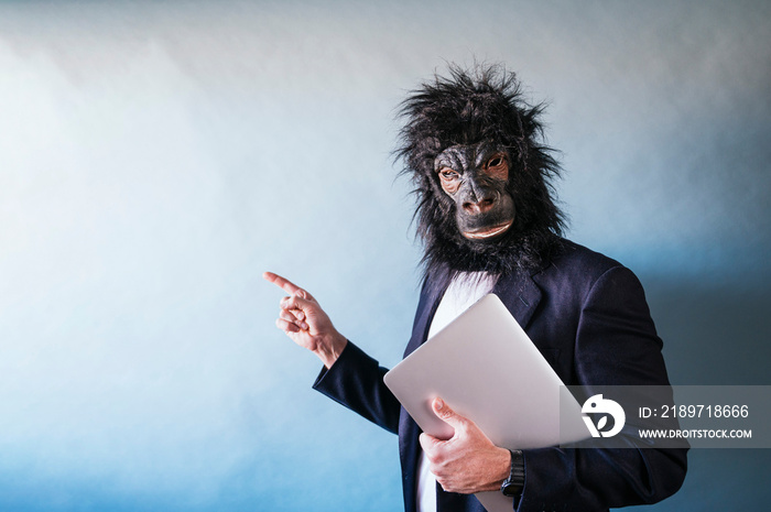 Man in gorilla mask with laptop under his arm and pointing with his finger laterally