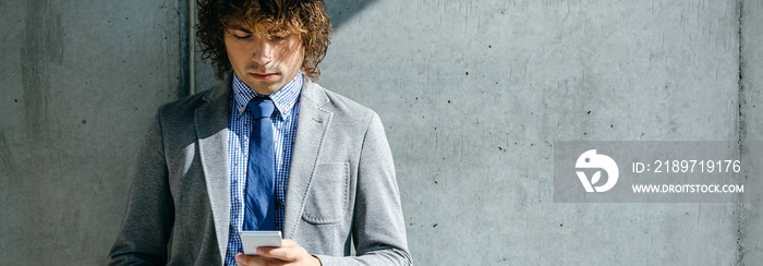 Businessman using mobile leaning on a concrete wall