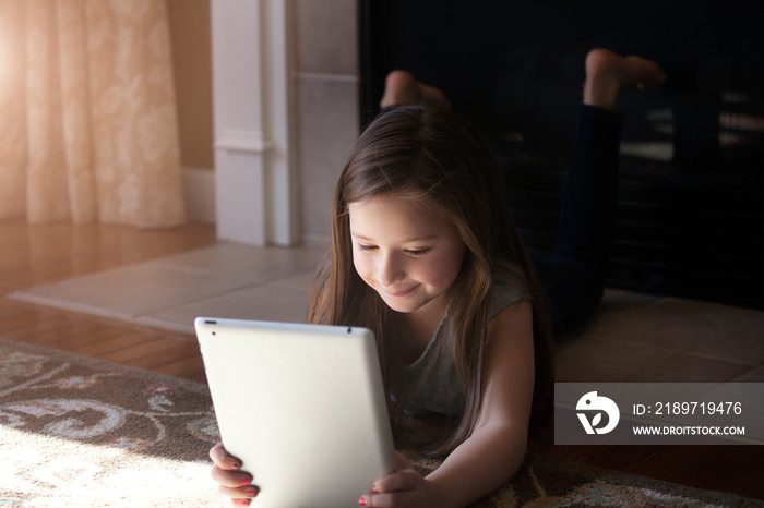 Girl (2-3) lying on floor and using tablet pc