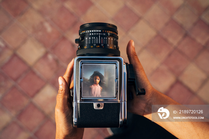 Looking down on an old camera, taking a photo of a young afro girl