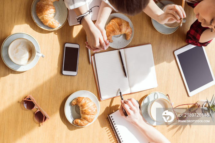 overhead view of young women sitting at coffee break with digital devices, business lunch