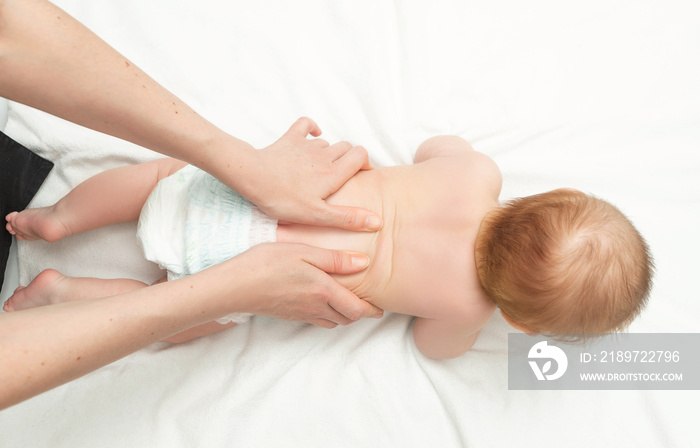 The baby is 5 months old, lying on his tummy. Mom gives back massage to the child, for its developme