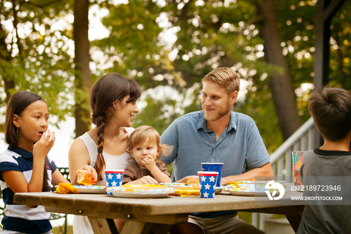 Family with kids (6-7,8-9, 12-17 months) eating lunch at picnic table