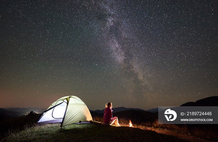 夏季夜间休息的女性徒步旅行者在篝火旁的山上露营，照亮了游客t