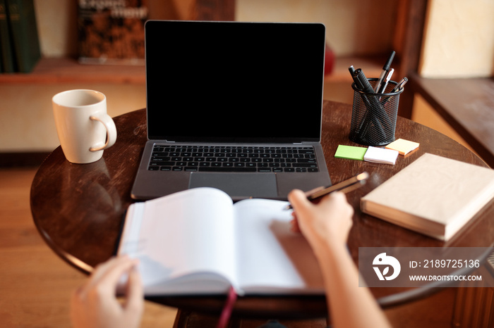 Woman sitting at desk using laptop with blank screen, mockup