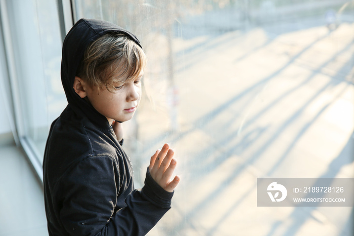 Homeless little boy near window indoors